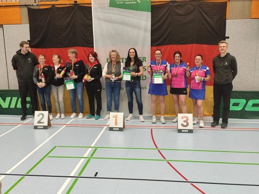 Drei Teams stehen auf dem Podium mit Medaillen in einer Sporthalle.